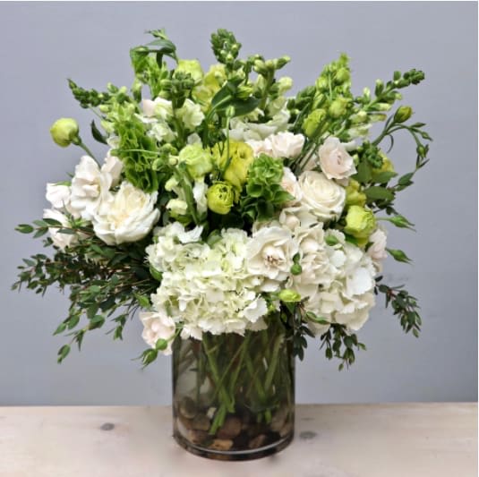 Tall arrangement of white hydrangeas and roses with bright green accents in a clear glass cylinder vase