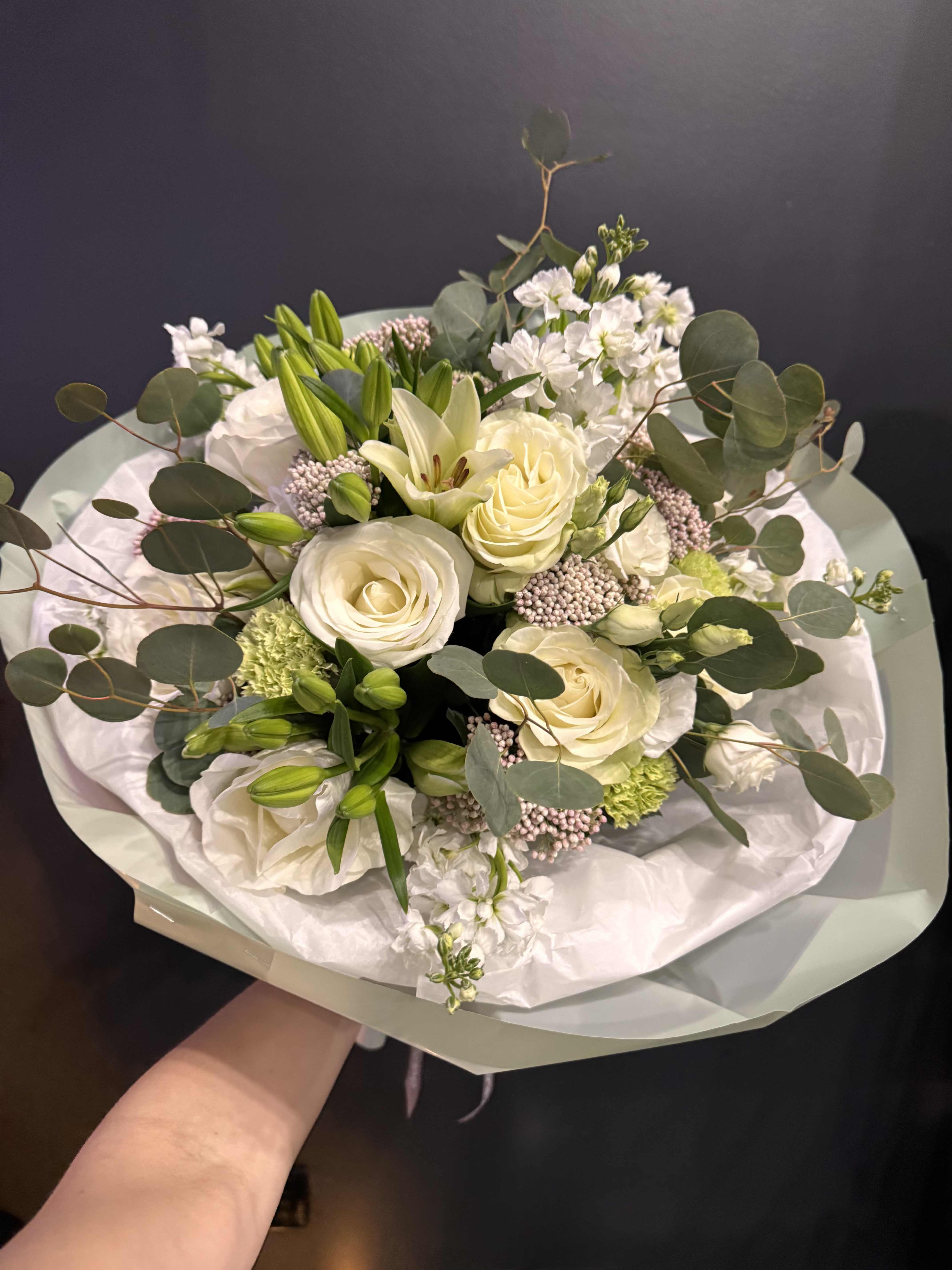 Ivory Whisper - A timeless and elegant arrangement featuring creamy ivory roses, fresh lilies, and delicate seasonal blooms, complemented by soft eucalyptus and airy textures. Designed in a natural garden style, this bouquet feels light, sophisticated, and effortlessly luxurious. Perfect for birthdays, anniversaries, sympathy, or simply to express refined taste and care.