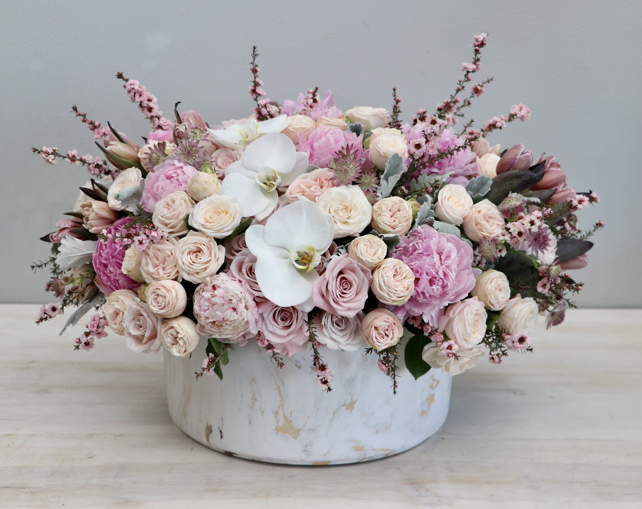 Low arrangement of blush roses, pink peonies, and white orchids in a round white ceramic vase