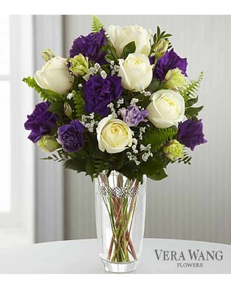 Arrangement of white roses and purple lisianthus in a clear glass vase with a jeweled band.