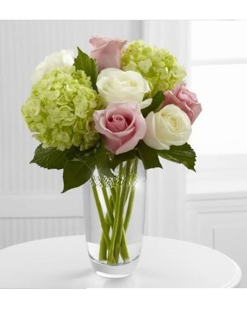 Arrangement of pale pink roses, white roses, and green hydrangeas in a clear glass vase