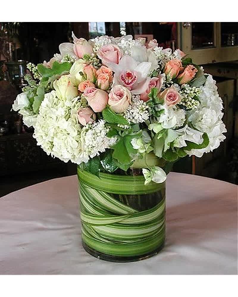 Round arrangement of white hydrangeas and pale pink roses in a clear vase lined with green leaves