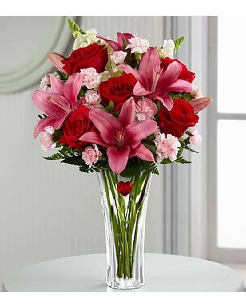 Tall clear vase of red roses, pink lilies, and light pink carnations in a mixed bouquet