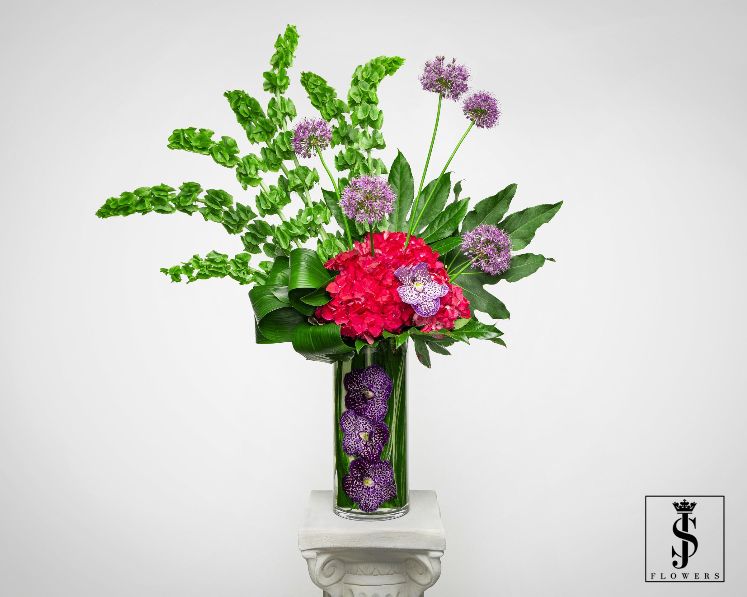 Tall modern arrangement with green bells of Ireland, pink hydrangea and purple orchids in a glass vase
