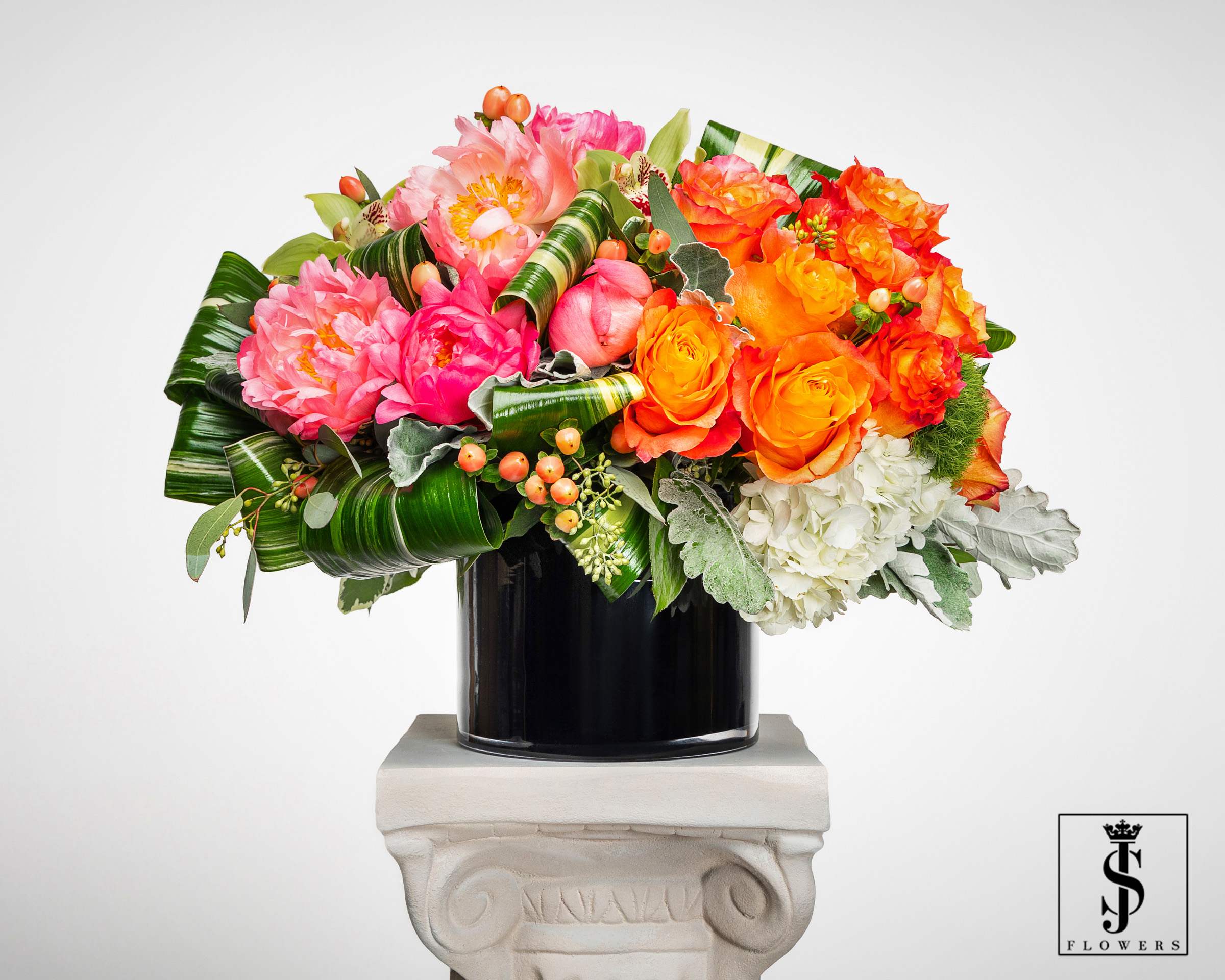 Bright pink peonies, orange roses, and white hydrangeas in a black cylinder vase