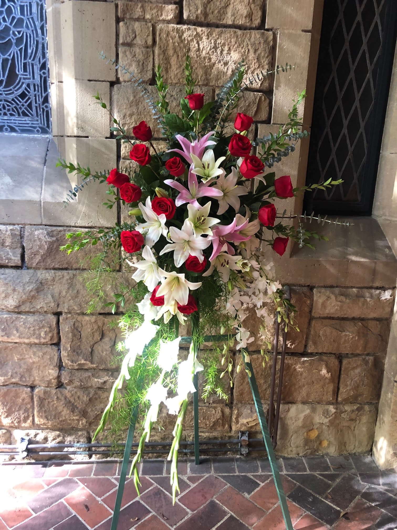 Red and White Standing Spray - Recipe: White Snapdragons, White Orchids, Red Roses, White Lilies, and Pink Stargazers on an easel. Availability: All year round Design View: Front Facing View Photo shown: Standard