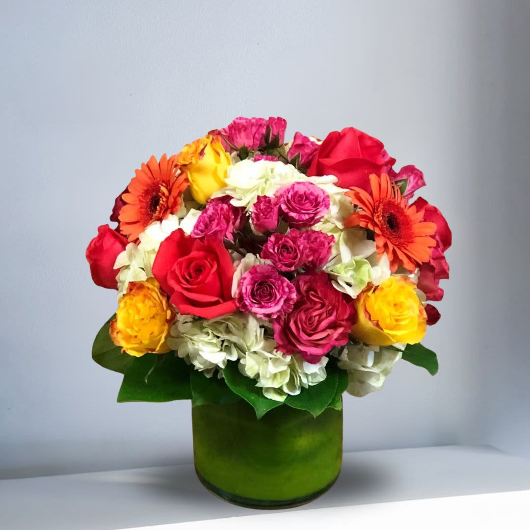 Here Comes the Sun - Type of Flowers: White Hydrangeas, Orange and Pink Roses, Orange Gerbera Daisies, Pink Spray Roses, and greens in a short vase with a leaf wrap. Availability: All year round Substitute Available: Yes Design View: All Facing View Photo shown: Regular 