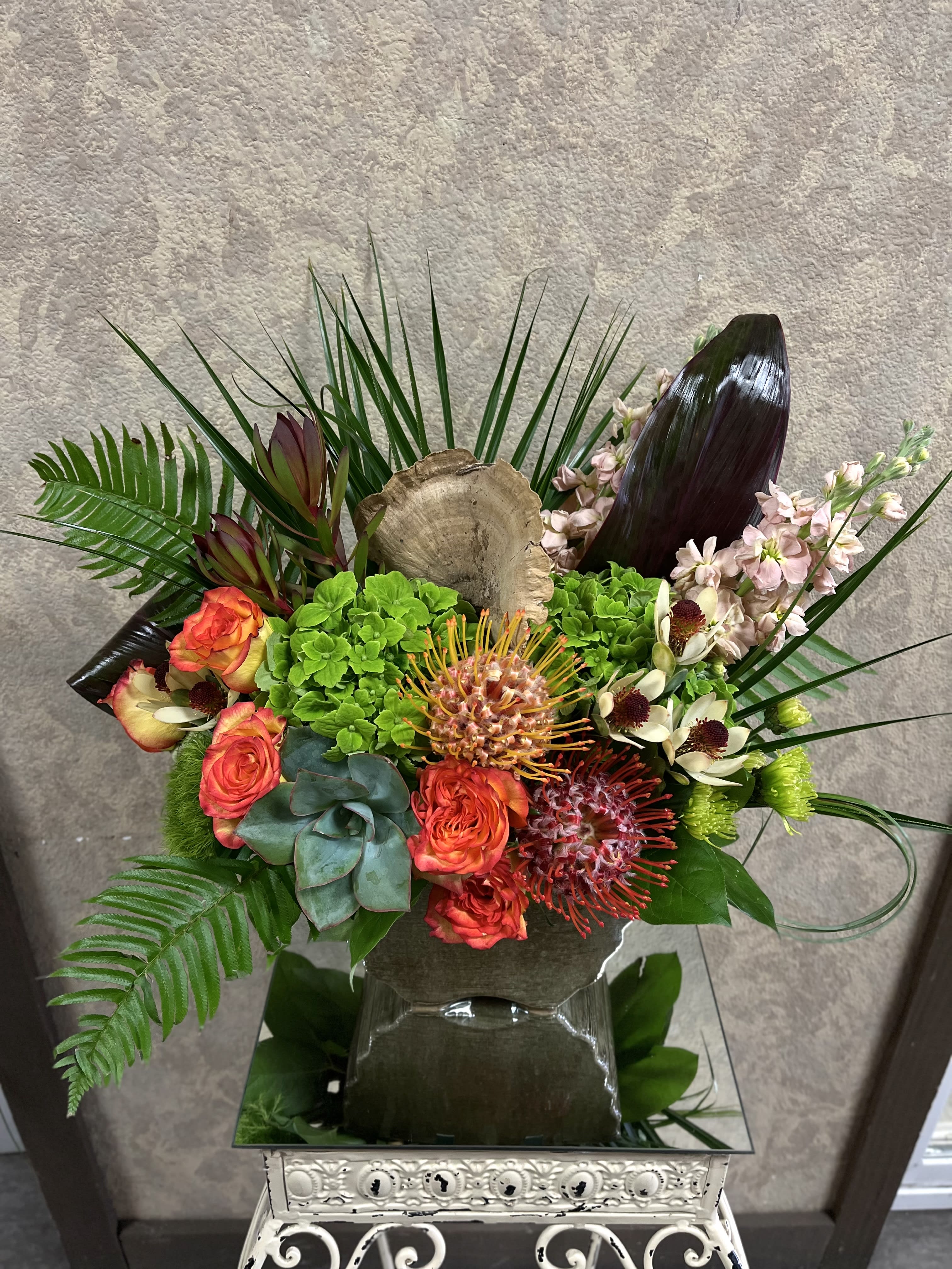 Sunset in Hawaii - Recipe Orange Roses, Green Hydrangeas, Protea, Beige Stock, Safari, Dianthus Barbatus, Chrysanthemums, Succulent and Tropical Greens in a porcelain vase.  Availability: All year round Substitute Available: Yes Design View: Symmetric Front Facing View Photo shown: Regular
