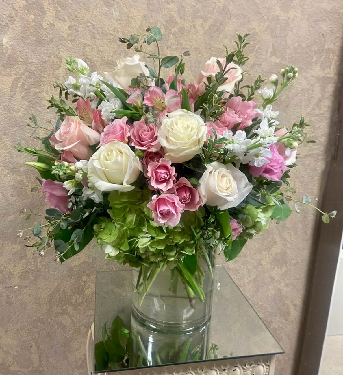 Fade Into You - Type of Flowers: Pink Spray Roses and Roses, White Roses, White Stock, Pink Lisianthus, Pink Alstroemerias, Green Hydrangeas, Fuji Mums and eucalyptus in a short, clear vase. Availability: All year round Design View: All Facing View Photo shown: Standard 