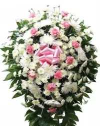 Soft Remembrance Standing Spray - A classic and elegant traditional standing spray designed to offer comfort and heartfelt sympathy. This graceful arrangement features white cushion mums, white spider mums, and soft pink carnations, beautifully accented with fresh greenery for a full and balanced presentation.  Finished with a pink ribbon bow, this timeless tribute symbolizes love, peace, and remembrance, creating a dignified and comforting display to honor and celebrate a cherished life.