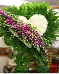 Serene Heart Standing Spray - A graceful and elegant standing spray featuring a solid heart of pristine white blooms, accented with a striking break of purple dendrobium orchids. This tasteful design combines classic symbolism with a touch of modern color, creating a heartfelt and visually memorable tribute.