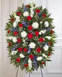 Stars &amp; Blooms Standing Spray - A bold and elegant oval standing spray designed to make a lasting impression. This vibrant arrangement features soft white spider mums and asters, striking blue delphinium, and rich red carnations and roses for a patriotic color palette. Accented with white stock and lush fresh greens, the design offers texture, fullness, and a refined sense of balance, creating a dignified and visually stunning tribute.