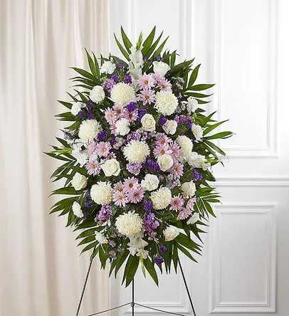 Lavender &amp; White Funeral Standing Spray - A serene and elegant lavender and white standing spray, thoughtfully arranged to convey peace, comfort, and remembrance. This graceful tribute features a harmonious mix of lavender and white roses, chrysanthemums, and stock, accented with lush greenery for a full and balanced presentation.  The soft lavender and white tones symbolize grace, sympathy, and everlasting love, making this arrangement a beautiful and heartfelt way to honor a cherished life. Perfect for display on a standing easel, it offers a dignified and comforting expression of sympathy.