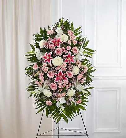 Blushing Stargazer Standing Spray - A stunning and elegant standing spray featuring a soft and romantic pink and white palette. This graceful arrangement includes fragrant stargazer lilies, pink roses, pink spray roses, pink carnations, white cremon mums, pink mini carnations, pink wax flowers or asters, and white stock or snapdragons, all accented with lush greenery for a full and balanced display.  The combination of pink and white blooms symbolizes love, admiration, and remembrance, making this arrangement a thoughtful and heartfelt tribute. Perfectly designed for a standing easel, it offers a beautiful way to honor a cherished life with elegance and grace. 