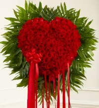 Heart’s Tribute - A striking and heartfelt standing spray designed to convey deep emotion and remembrance. This elegant arrangement features a dramatic red rose “bleeding heart” design, accented with lush fresh greens for depth and texture. A coordinating red bow adds a polished and thoughtful finishing touch, creating a powerful and visually