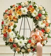 Serene Peach Tribute Wreath - A graceful and elegant solid peach wreath, thoughtfully designed to convey warmth and remembrance. This arrangement features a lush base of soft peach blooms, including delicate peach carnations, elegant peach lilies, and charming peach spray roses. Accented with complementary peach-toned florals for added depth and texture, the design offers a soothing and comforting presence. Finished with a beautifully coordinated peach bow, this wreath creates a heartfelt tribute, perfect for expressing sympathy, love, and gratitude.