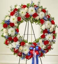 Patriotic Remembrance Standing Wreath - A dignified red, white, and blue standing wreath designed to honor and remember a cherished life. This beautiful tribute features a vibrant mix of red, white, and blue flowers, thoughtfully arranged with fresh greenery to create a full and respectful display.  Finished with a tri-color ribbon bow, this wreath symbolizes honor, remembrance, and patriotic pride, making it a meaningful tribute for funeral or memorial services, especially for veterans or those who proudly served