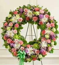 Garden Tribute Standing Wreath - A beautiful standing wreath featuring a soft garden-inspired blend of colors and textures. This elegant tribute includes green spider mums, white spider mums, green button mums, pink roses, lavender carnations, pink carnations, and green carnations, thoughtfully arranged with fresh greenery for a full and natural presentation.  Finished with a green ribbon bow, this wreath offers a graceful and heartfelt expression of remembrance, love, and sympathy, making it a meaningful tribute for funeral or memorial services.