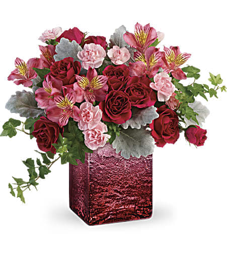 Red and pink roses, carnations, and alstroemeria in a red glass cube vase with trailing ivy
