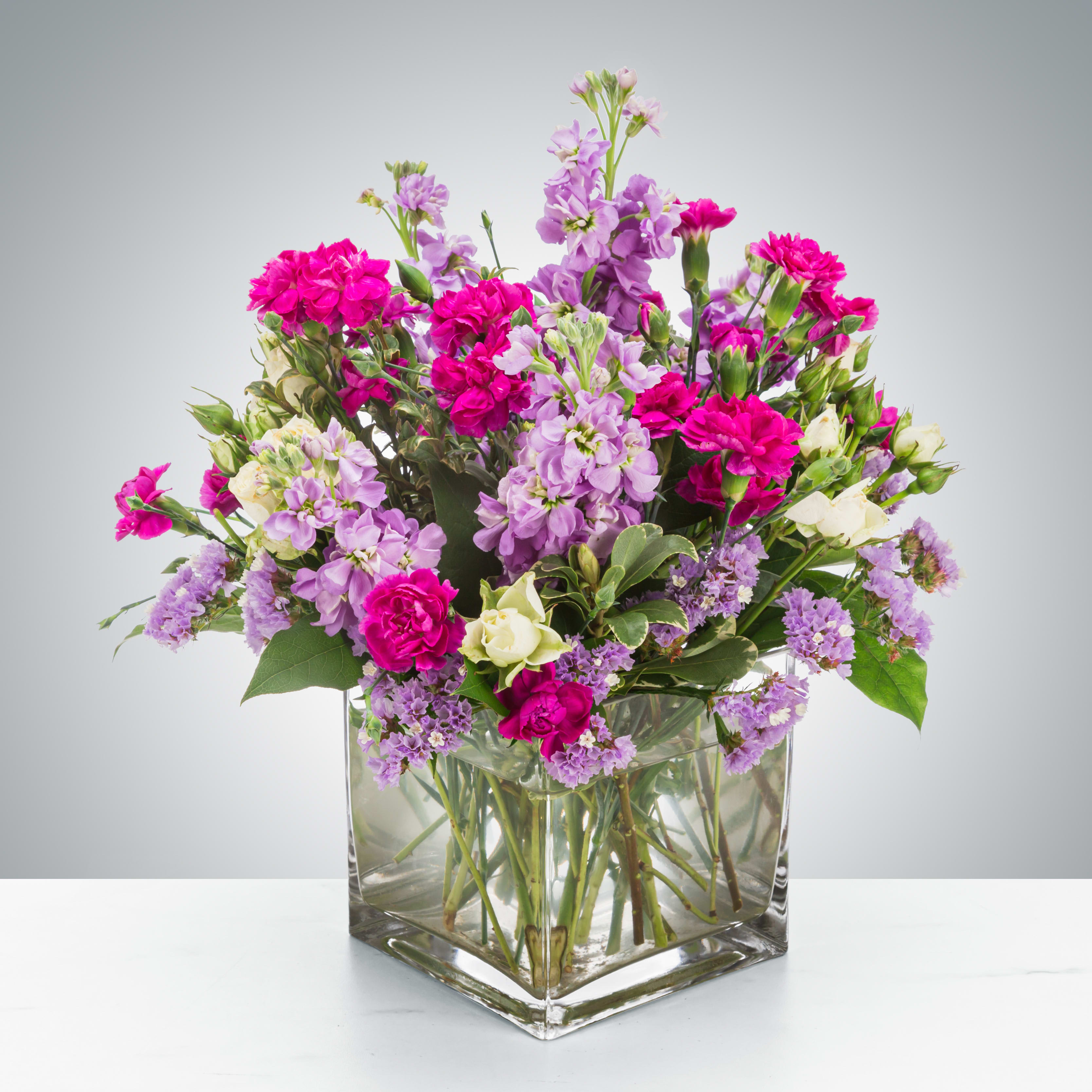 Cube vase arrangement of hot pink carnations, lavender stock, and white roses