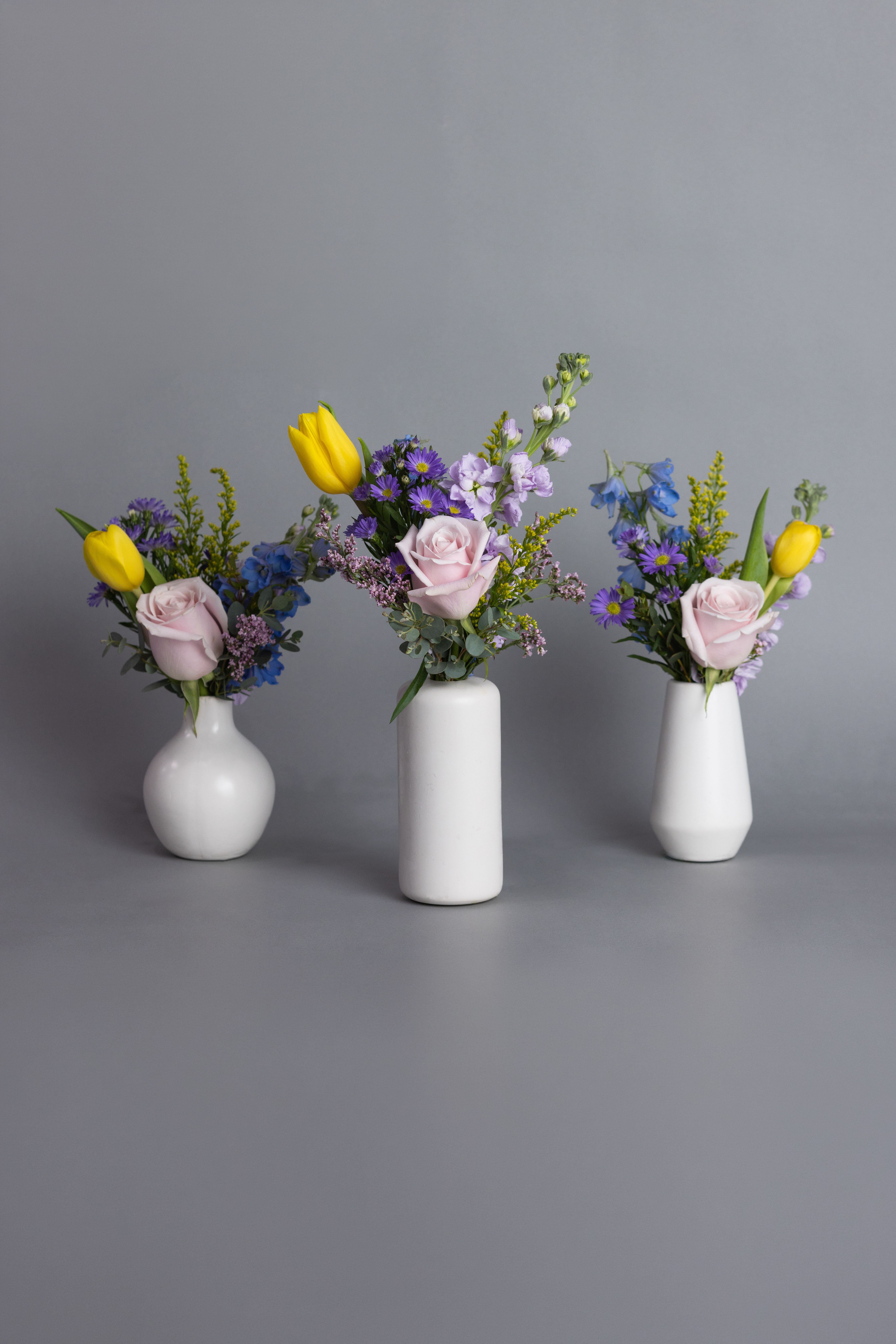 Sunday Brunch Trio - Celebrate the beauty of the season with a thoughtfully designed trio of bud vase arrangements, perfect for an Easter or Passover tablescape. This collection offers effortless versatility, allowing each petite arrangement to be styled together as a centerpiece or dispersed along the table for a more organic, layered look.  Featuring a delicate mix of seasonal blooms in soft, fresh tones, each vase highlights the natural charm of spring—light, airy, and inviting. The varying heights and textures create visual interest without overwhelming the table, making them ideal for intimate gatherings or larger celebrations alike.  Elegant in their simplicity, these bud vases bring a refined yet relaxed feel to your holiday table, complementing everything from classic linens to more modern settings while allowing space for conversation, dining, and connection.  Sold in set of 3. 