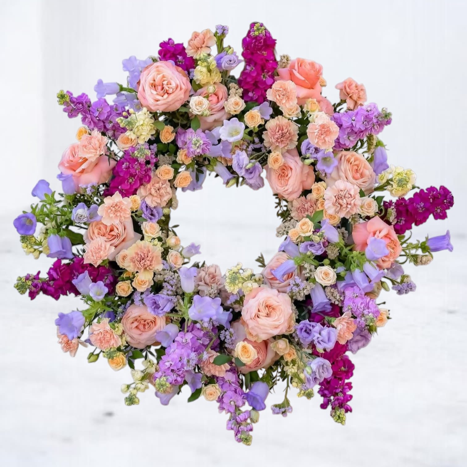 Pastel wreath of peach roses, carnations, and purple blooms in a full circular design.