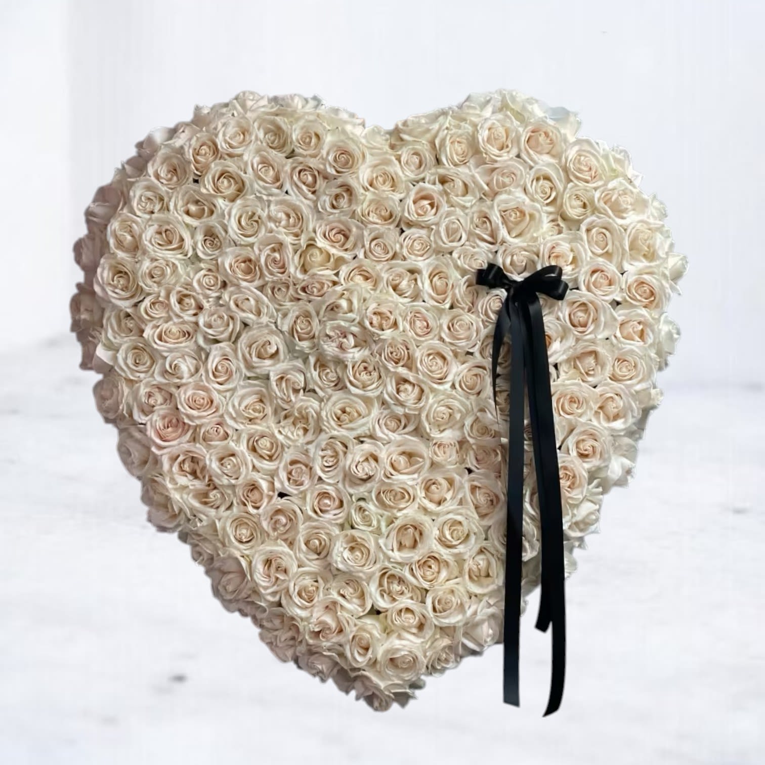 Heart-shaped arrangement of cream roses with a black ribbon bow on one side