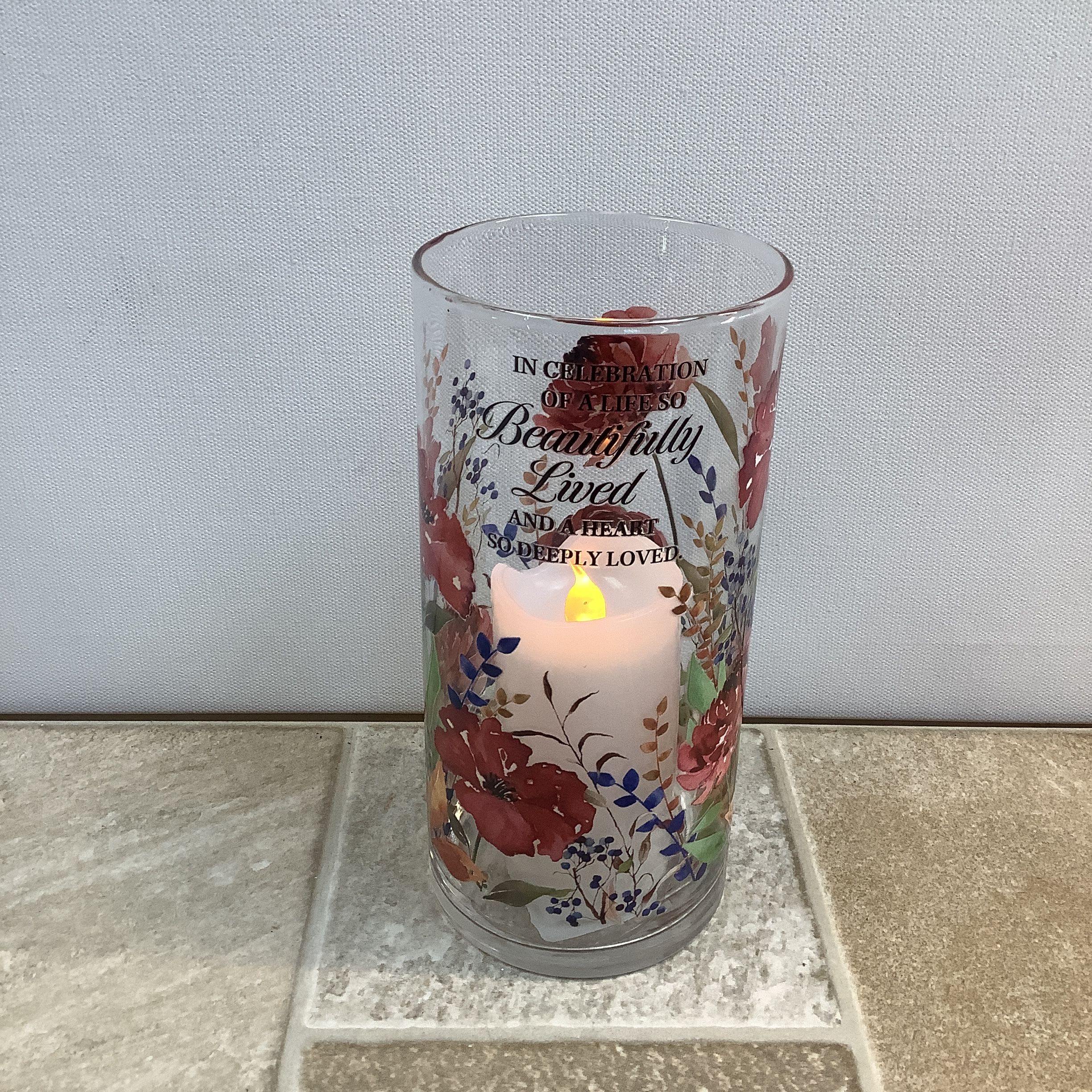 Lit memorial candle in a floral glass holder