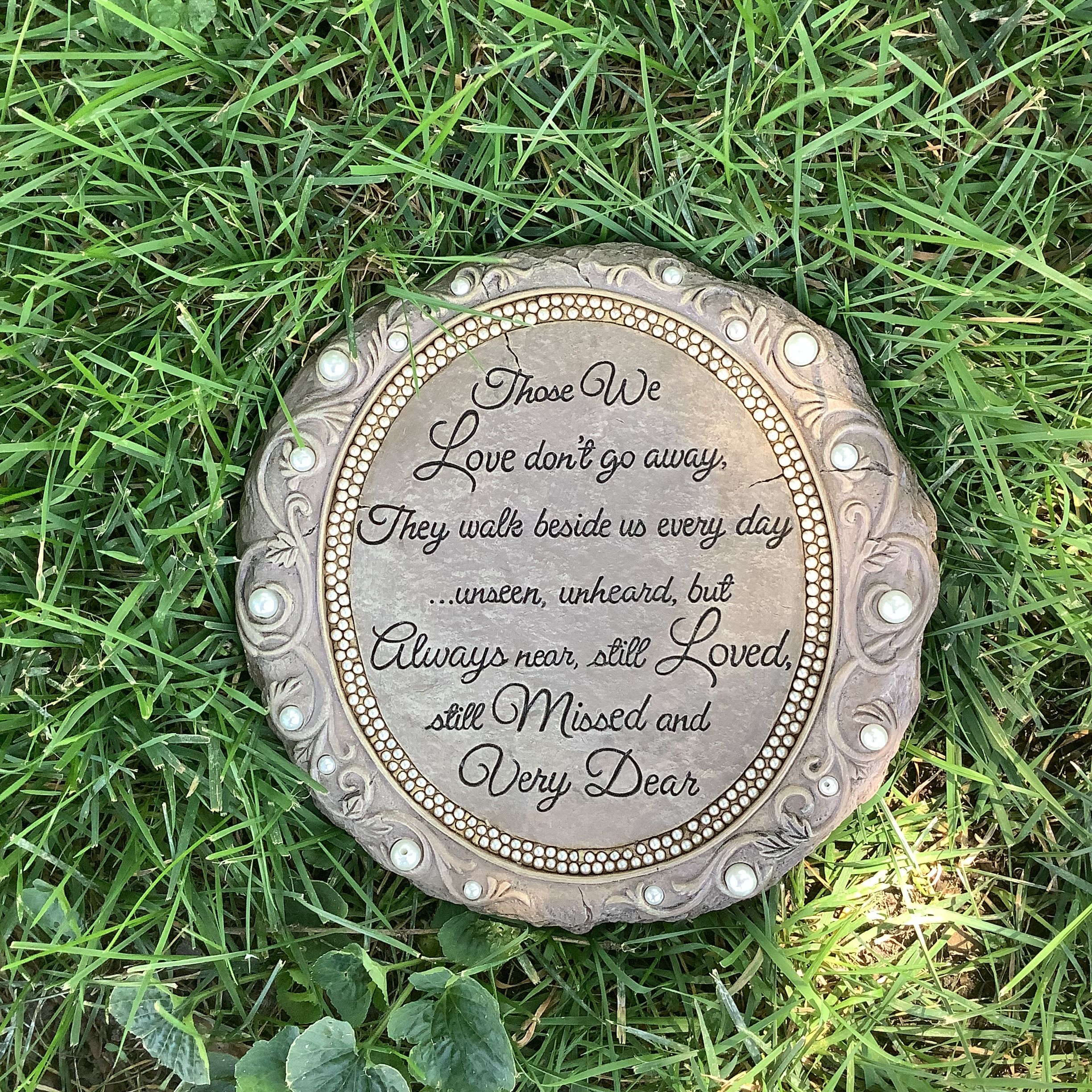 Round memorial plaque with engraved text lying in grass