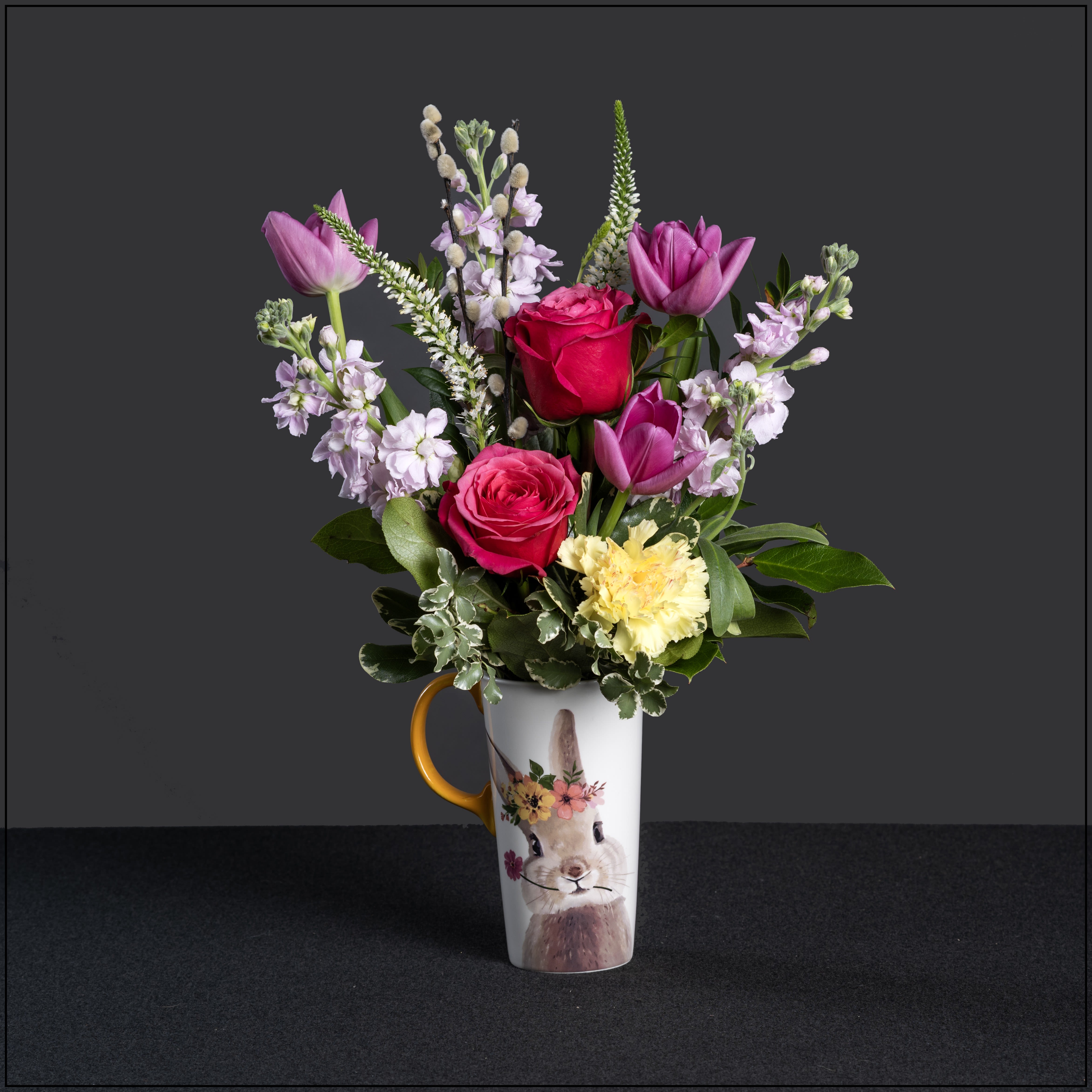 Pip - Here comes the Easter bunny! A fun, oversized, and tall mug, with the cutest bunny painting, filled with stock, roses, tulips, carnations, veronica, and pussy willow. Approximately 17" tall and 13" wide.