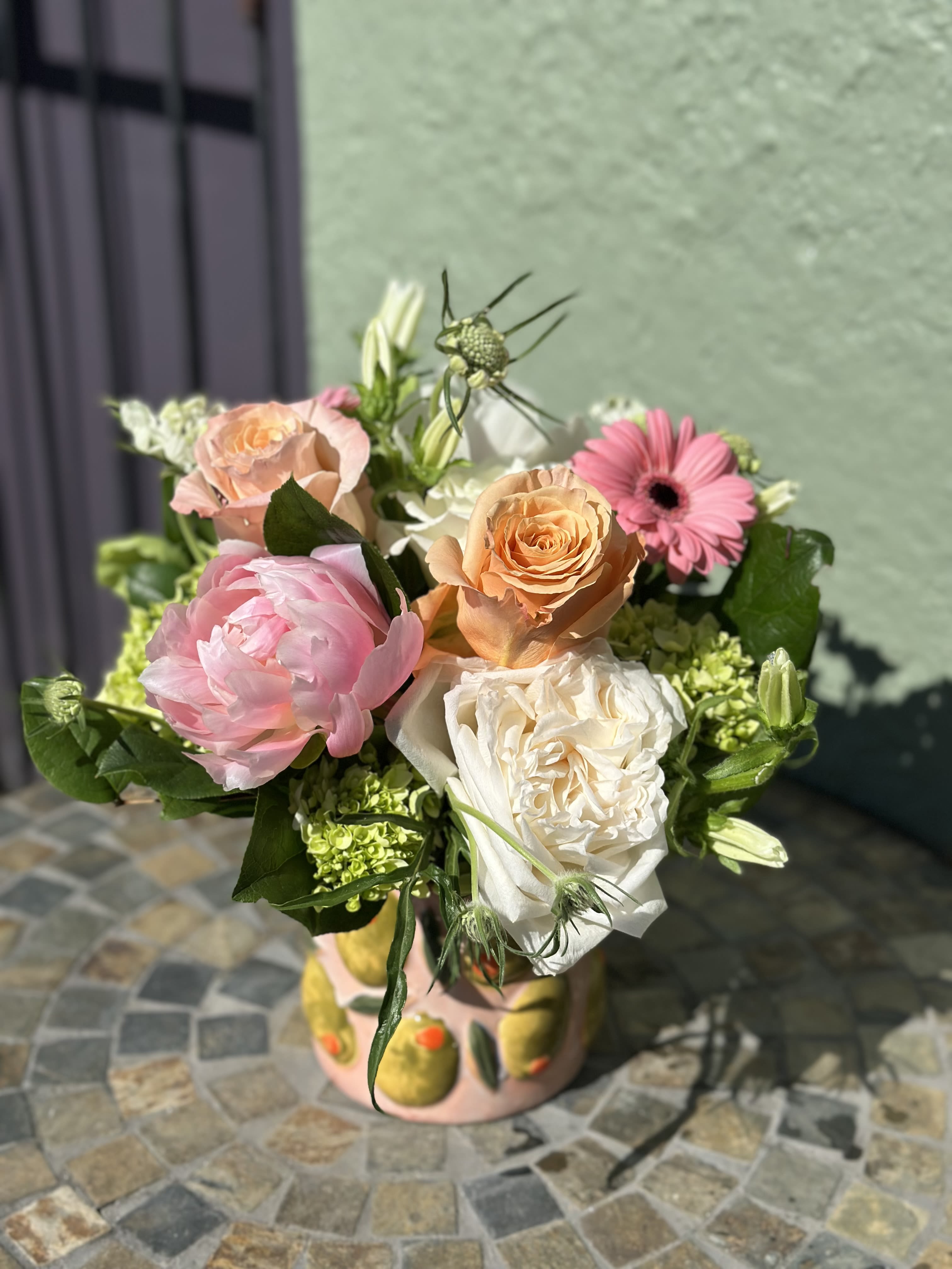 Martini - Meet Martini, a playful, stylish design that brings a splash of charm to any space. Set in a chic ceramic pot adorned with whimsical olive details, this arrangement features pink, peach, and white blooms. It feels like a nod to your favorite classic cocktail: crisp, fresh, and fun! 