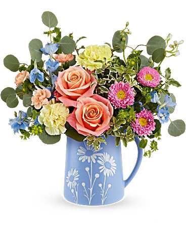 Mixed bouquet of peach roses and colorful blooms in a blue daisy-print pitcher