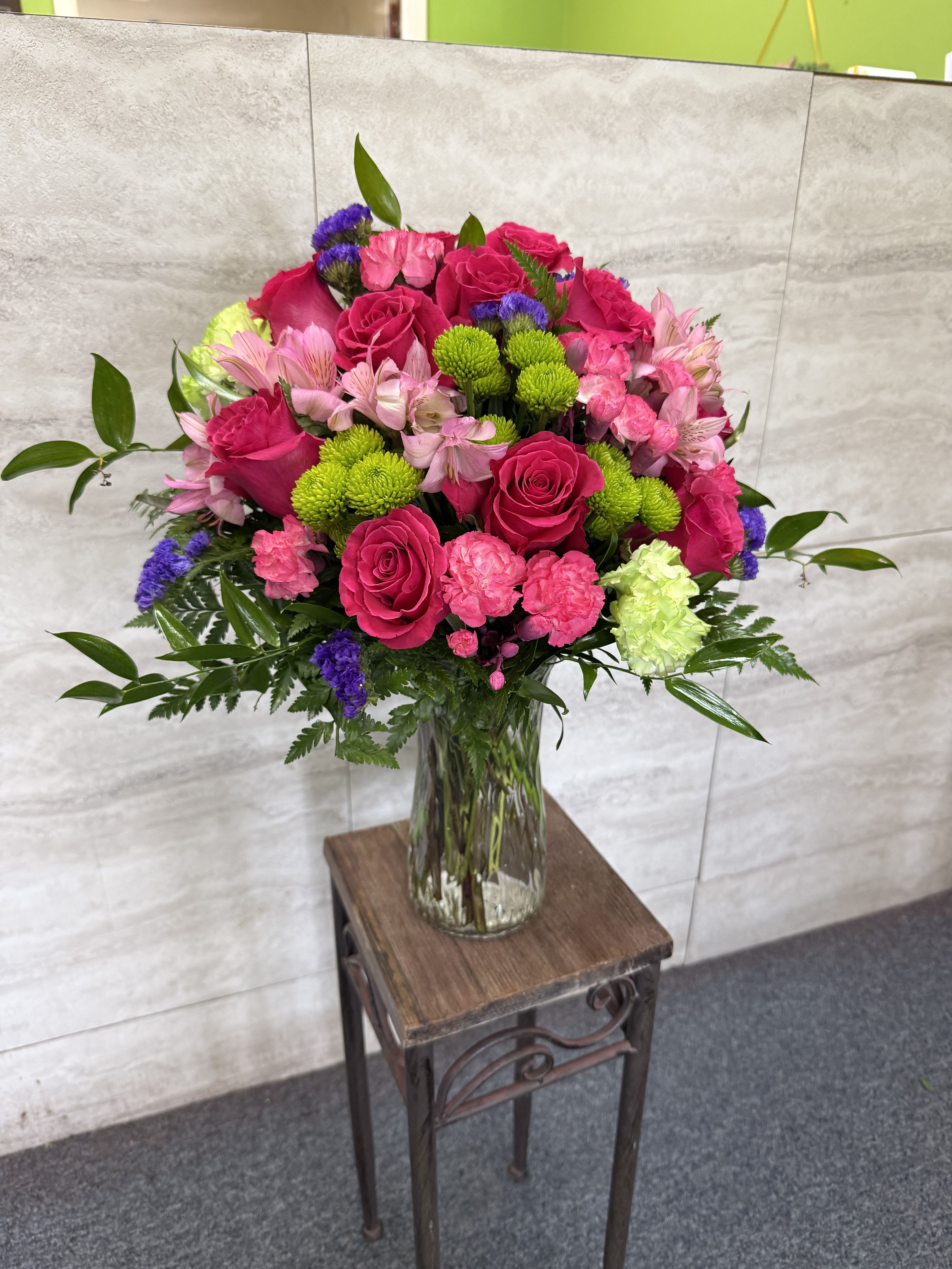 Bright pink roses, carnations, and mixed blooms in a clear glass vase on a small table