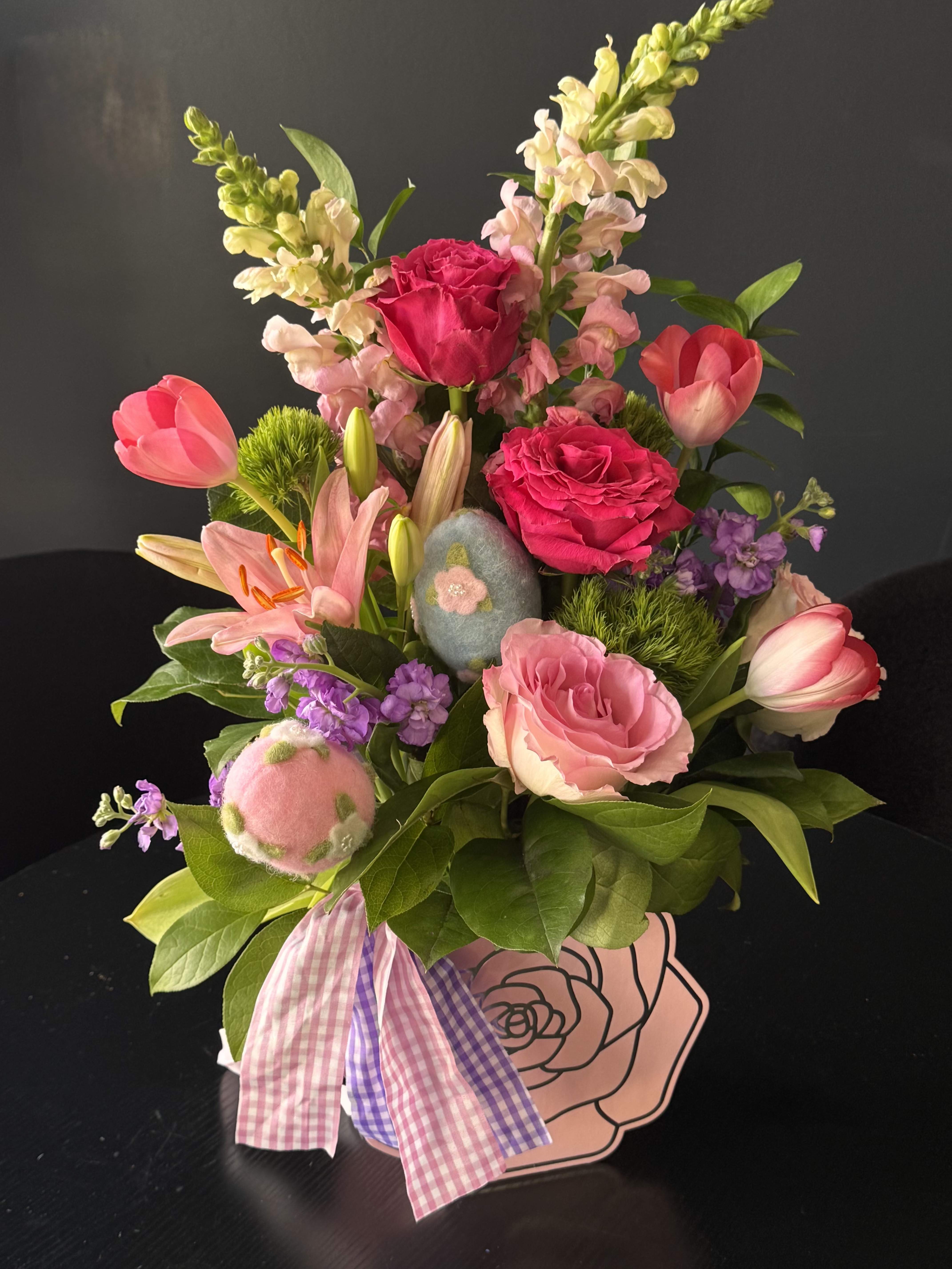 Easter Garden Delight - Easter Garden Delight is a vibrant spring composition designed to celebrate the beauty of the season. This arrangement features a delicate mix of pink roses, tulips, lilies, and seasonal blooms, complemented by fresh greenery and playful Easter details. Soft pastel tones blend with brighter floral accents to create a joyful and uplifting design. Decorative Easter elements add a charming, festive touch, making this arrangement perfect for holiday gifting or decorating your home. Designed in a stylish box, this piece feels modern, fresh, and full of life — a perfect way to celebrate Easter with elegance and color.