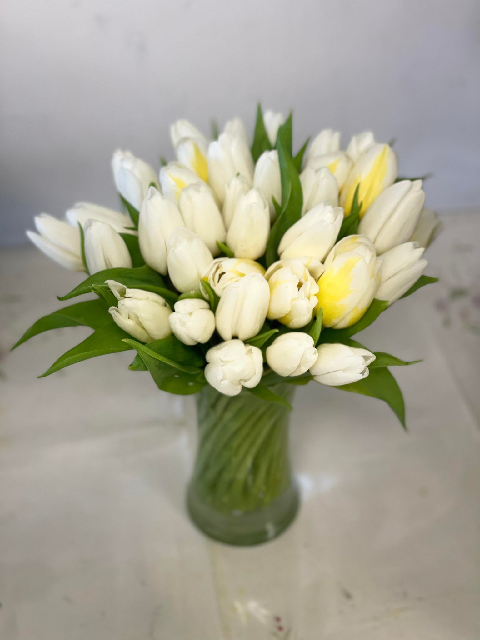Tight bouquet of white and pale yellow tulips arranged in a clear glass vase.