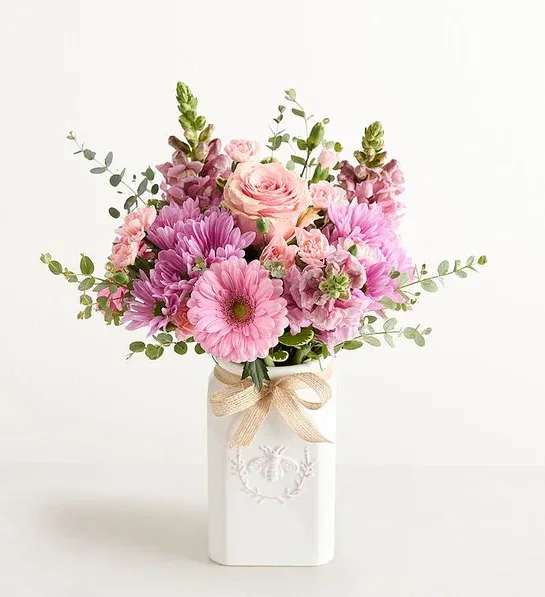 Pink and lavender flower arrangement in a white ceramic vase with a bow