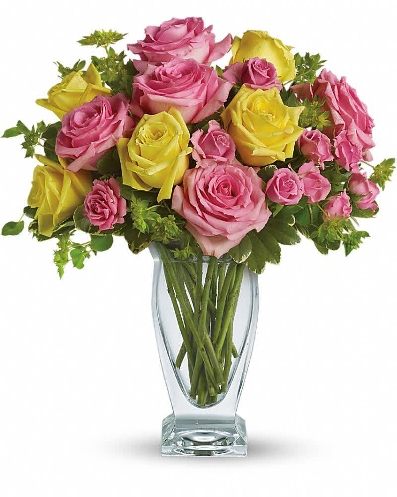 Tall clear vase of pink and yellow roses arranged in a mixed bouquet