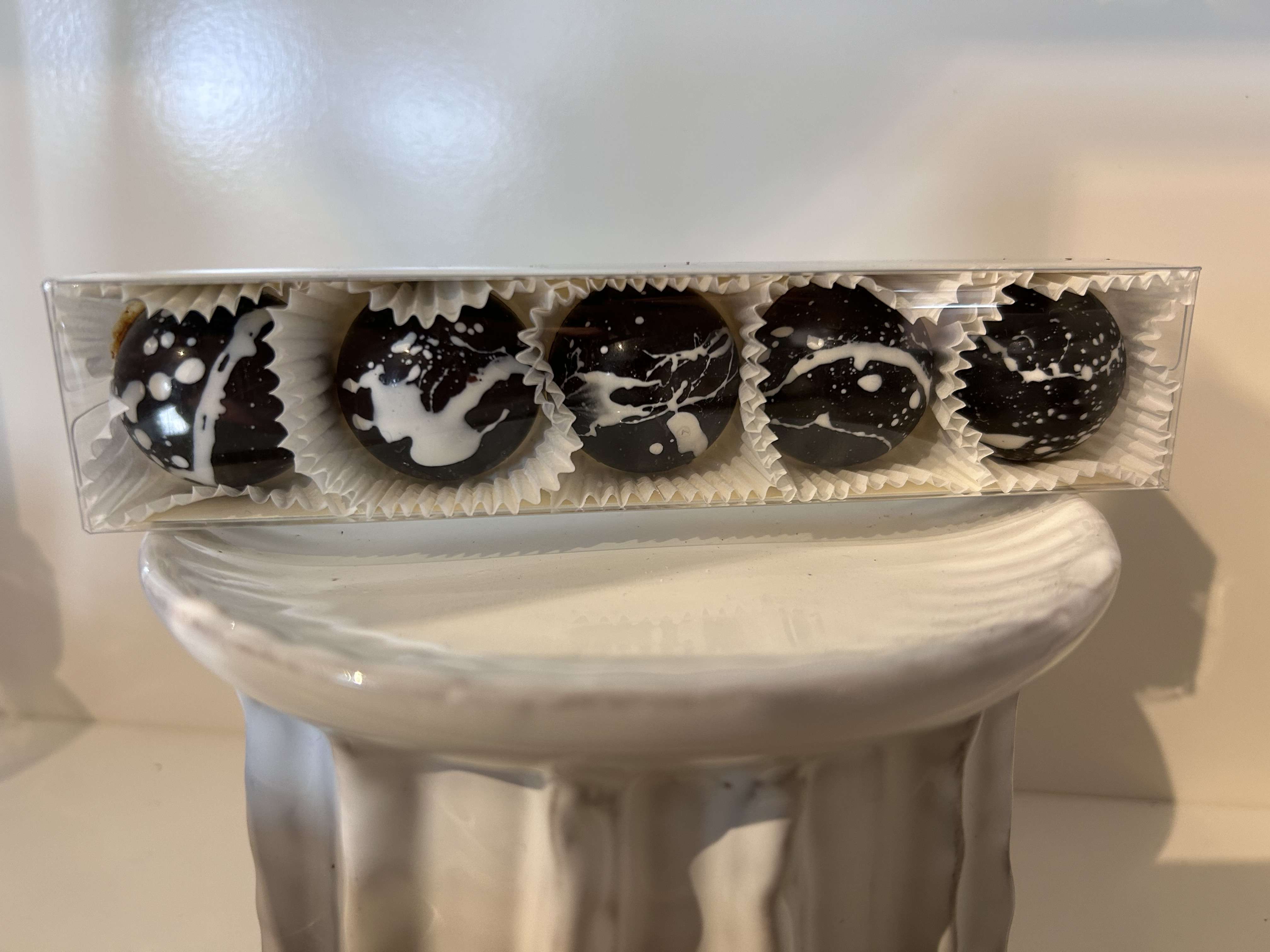 Box of five dark chocolate truffles with white splatter decoration on a white pedestal