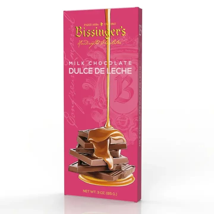 Pink boxed milk chocolate dulce de leche bar with caramel pouring over stacked chocolate pieces