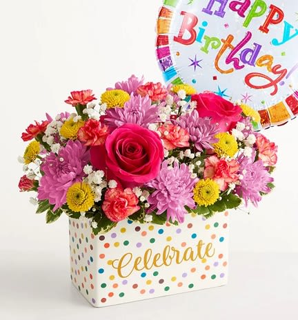 Celebrate the Day  - Mixed flowers sit low and full in a rectangular white ceramic container dotted in multicolored polka dots with "Celebrate" in gold script, giving the design a festive, gift-ready look that still fits easily on a dining table or desk.  Perfect for birthdays, milestone celebrations, or anyone who loves bright, whimsical color, this arrangement is the kind of gift that makes the recipient feel truly seen and celebrated. The low-profile design is easy to place and care for: keep blooms in fresh water, out of direct sun, and they'll keep bringing smiles through the celebration. Balloon included