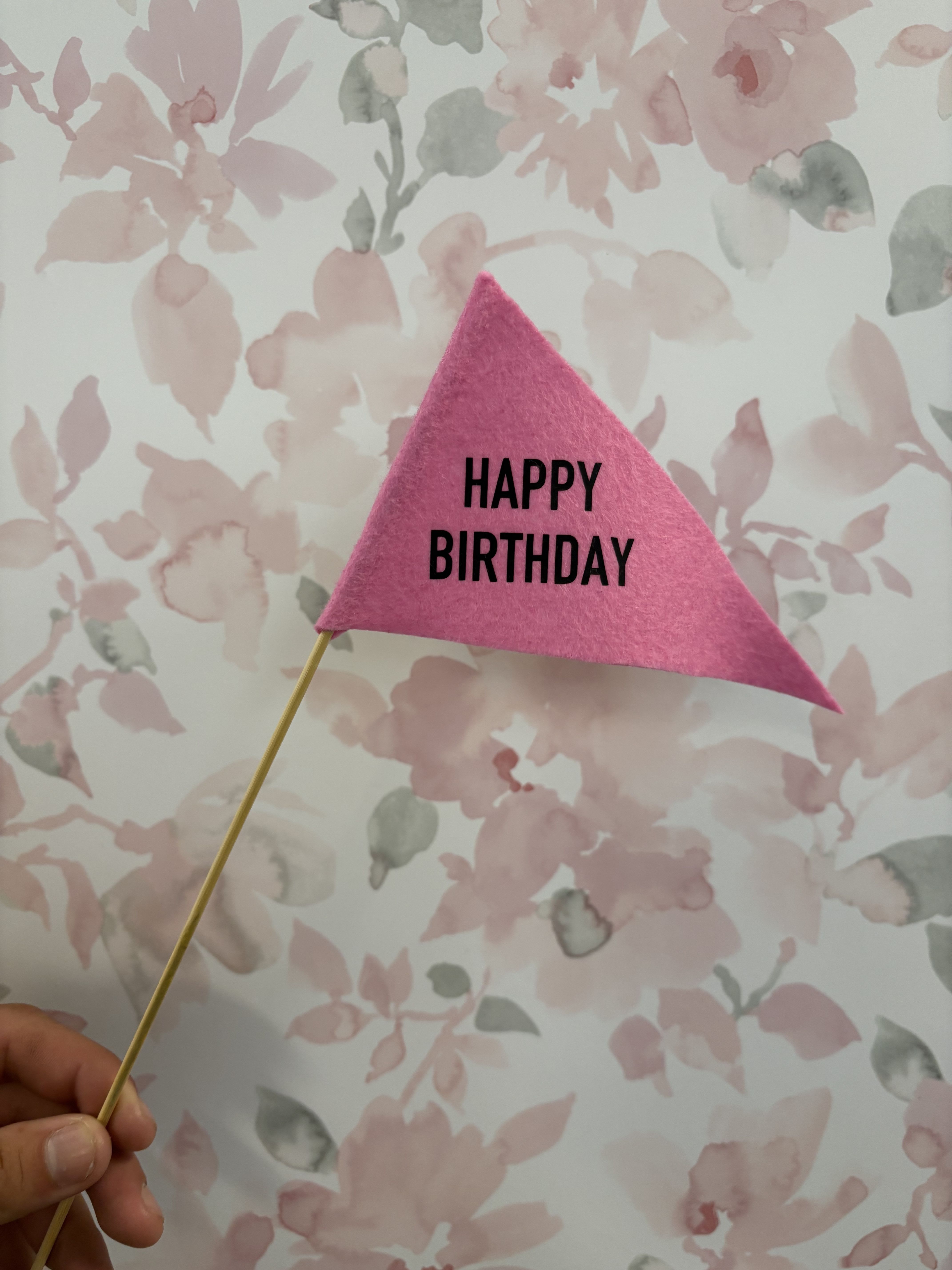 Pink felt birthday pennant on a wooden stick against a floral background