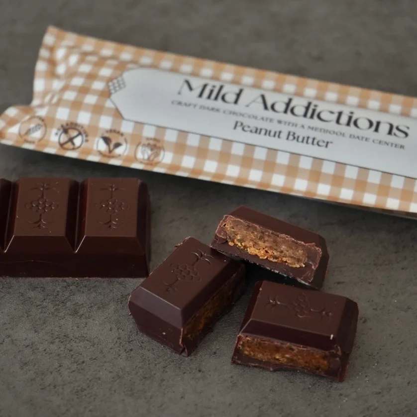 Unwrapped dark chocolate pieces with peanut butter filling beside branded wrapper.