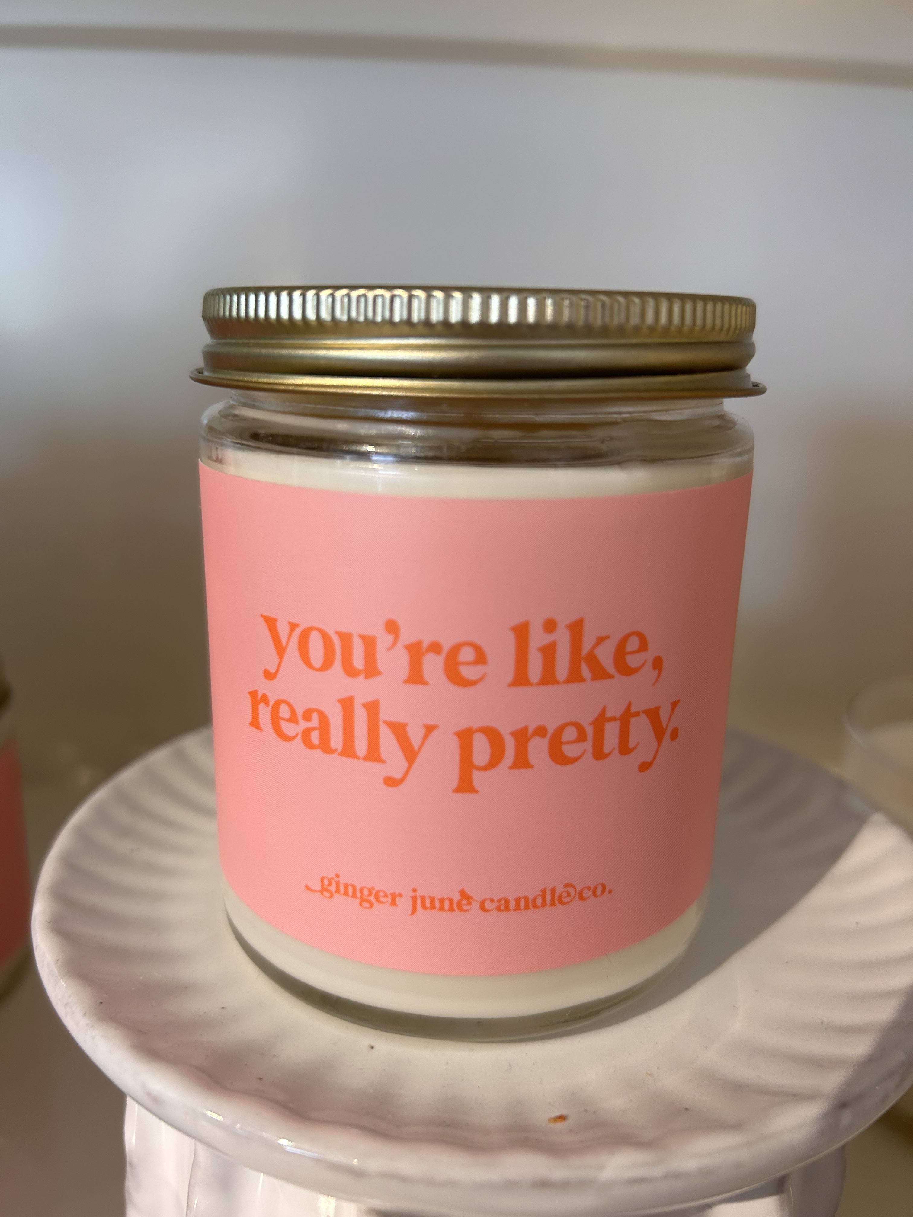 Pink-labeled jar candle with gold lid on a white ceramic pedestal stand