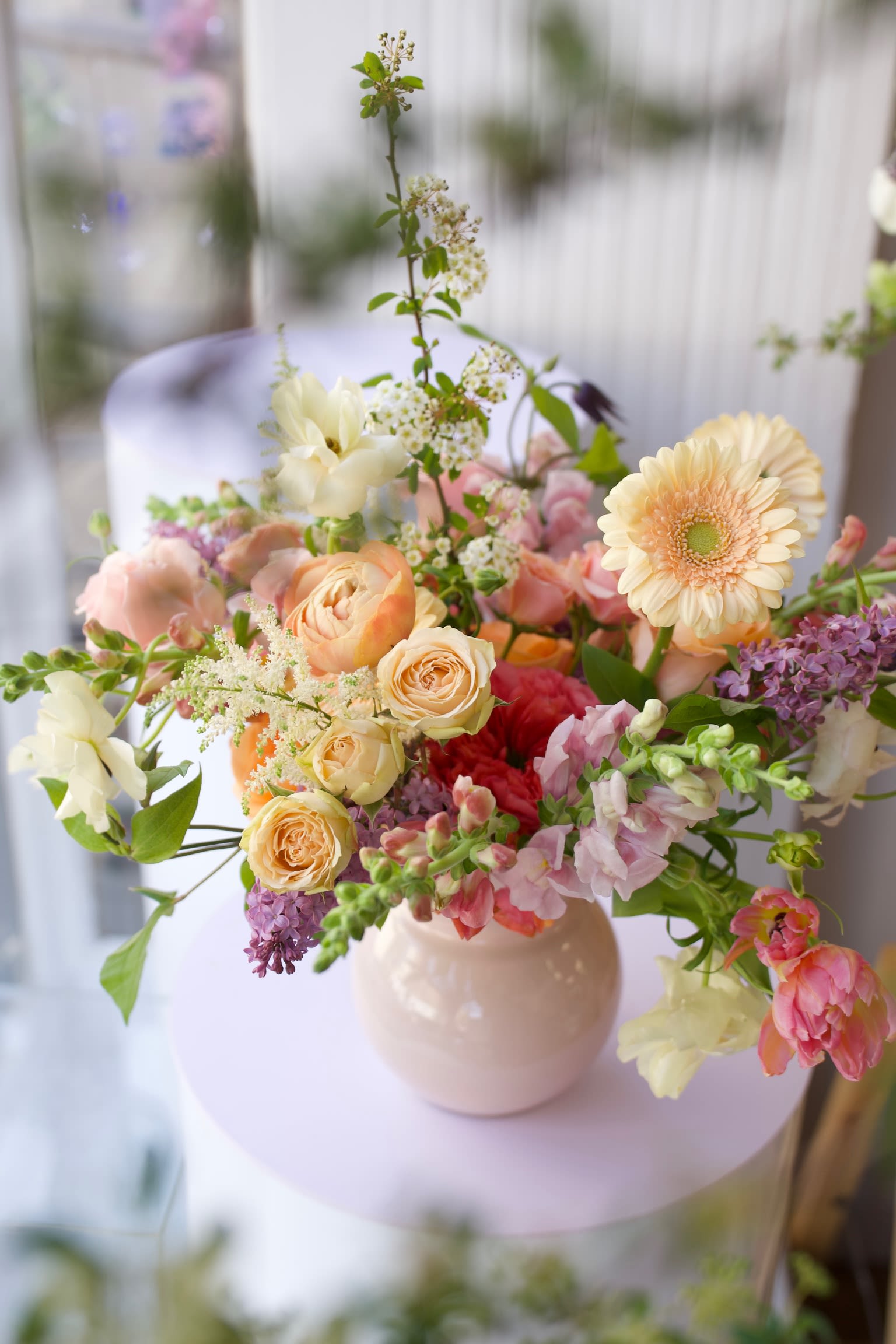 Daydream - A soft, garden-style floral arrangement featuring apricot garden roses, ranunculus, tulips, snapdragons, and delicate seasonal blooms in warm peach, blush, and buttery tones. Designed in a low ceramic vase with an airy, organic shape, this elegant spring arrangement brings a fresh, natural garden feel to any space—perfect for everyday styling, hosting, or thoughtful gifting.