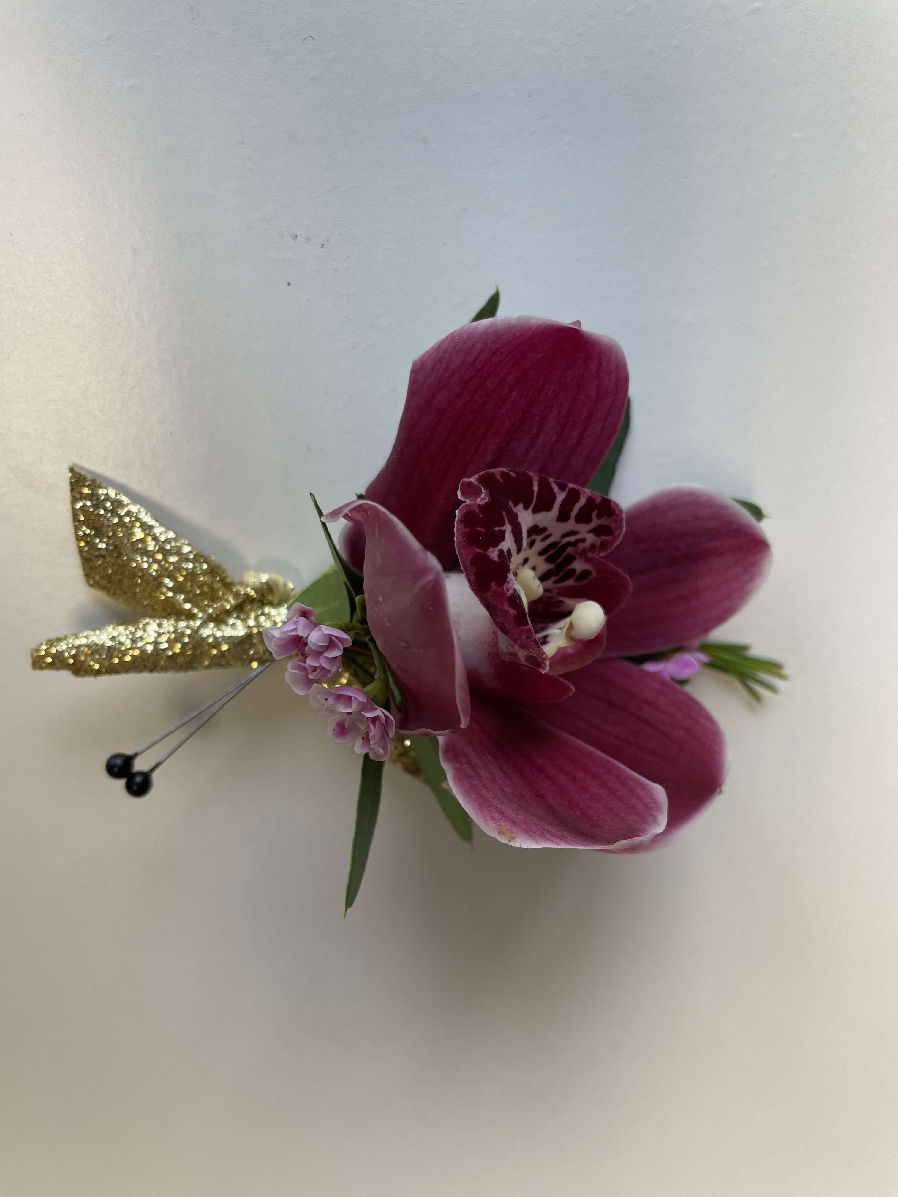 Magenta orchid corsage with small pink blooms and gold glitter accents on a white background