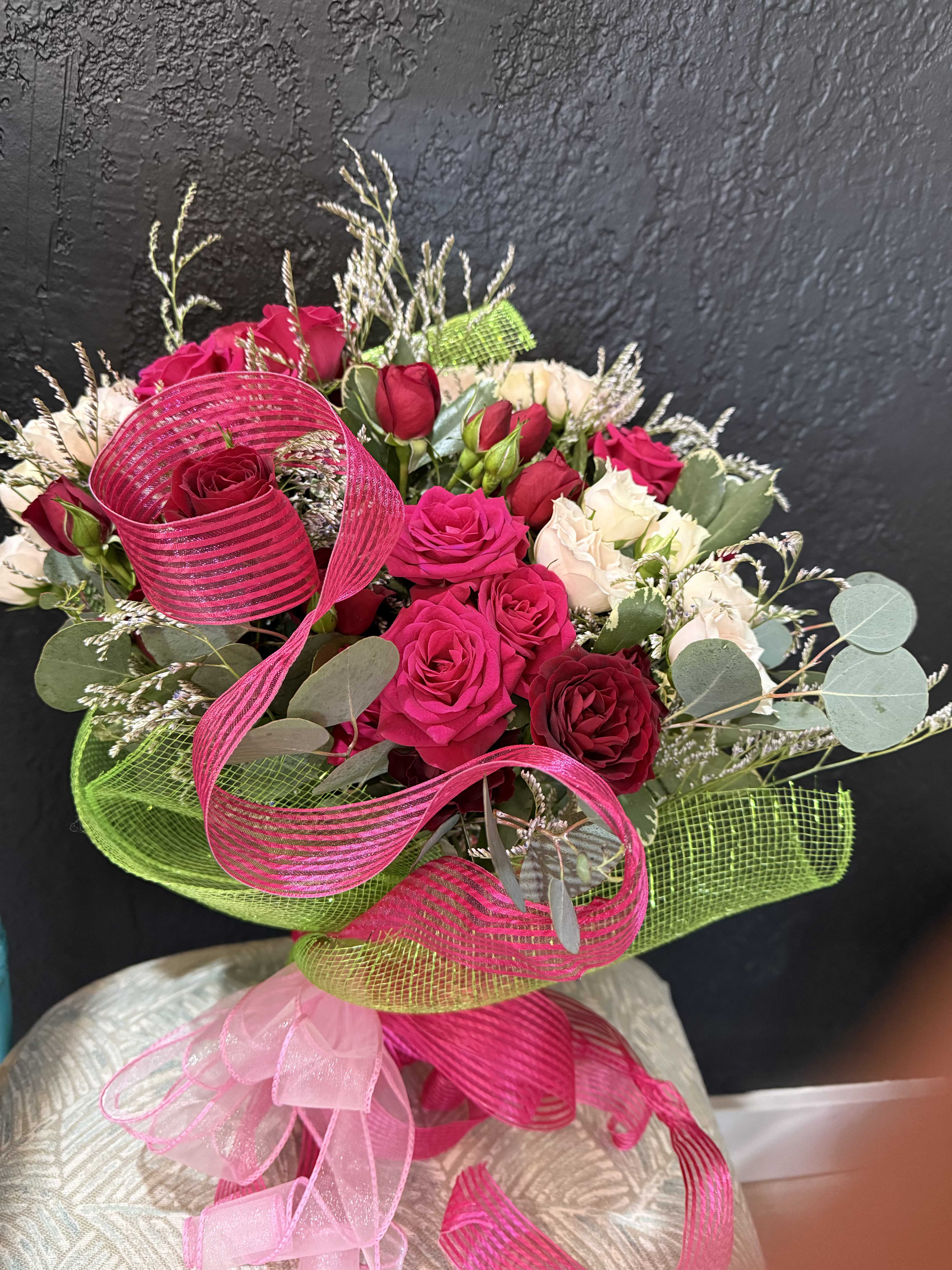 Hand-tied bouquet of red and cream roses wrapped in bright pink and green mesh with ribbon bow