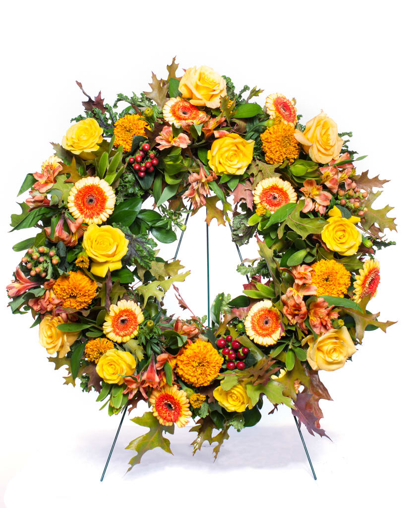 Autumn wreath of yellow roses, orange gerberas, and marigolds displayed on a metal stand