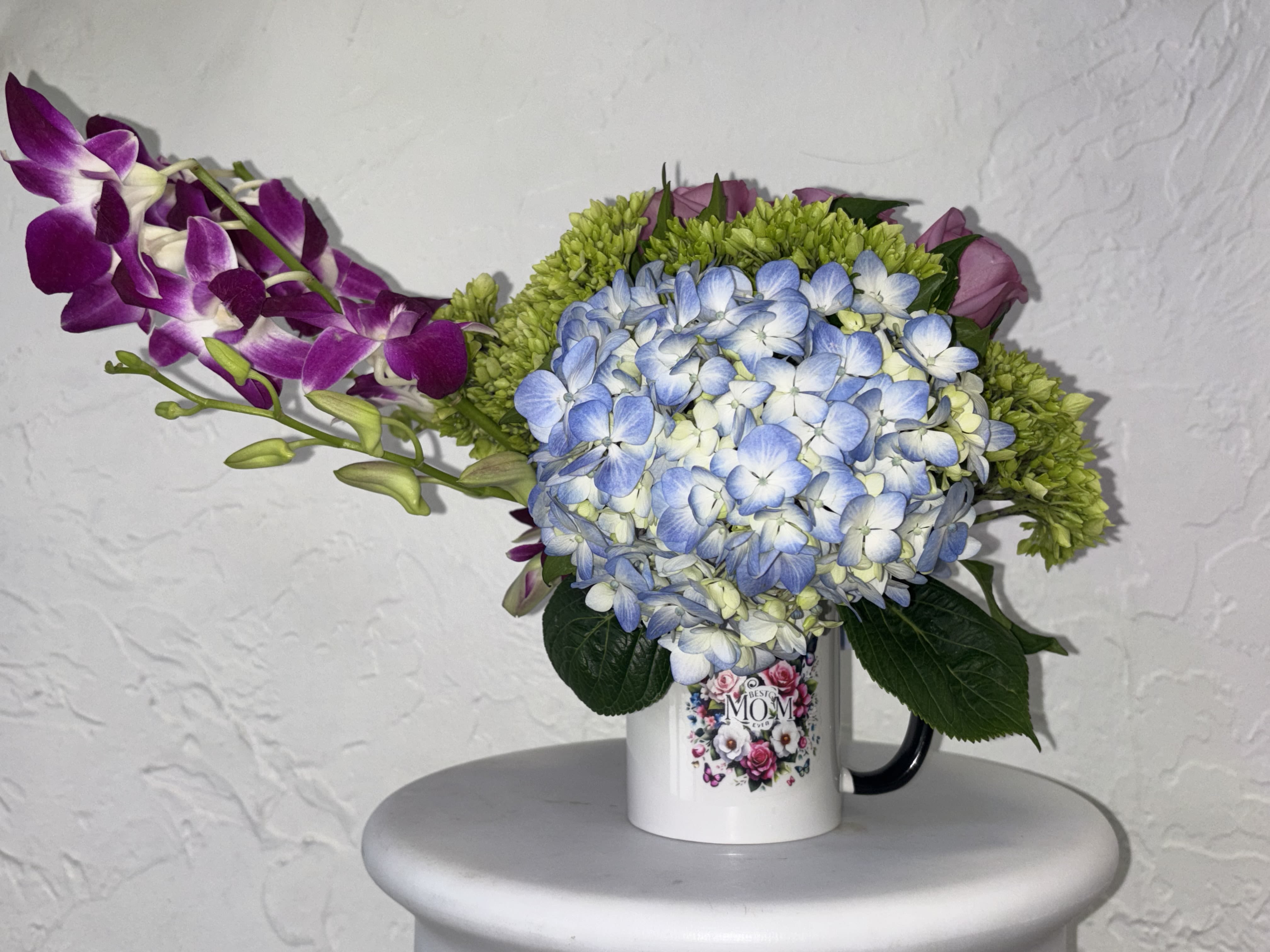 Morning Tea - Blue and green hydrangea come together, with lavender roses and orchids in a Mother's Day mug that  no mom can resist 