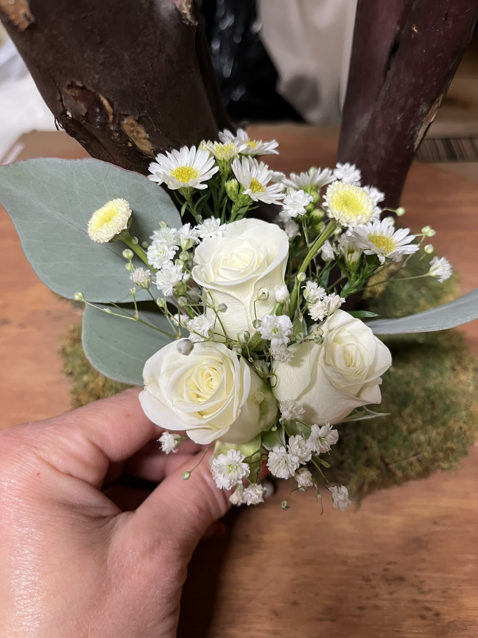 Small wedding boutonniere with white roses, tiny white daisies, and filler blooms held in a hand