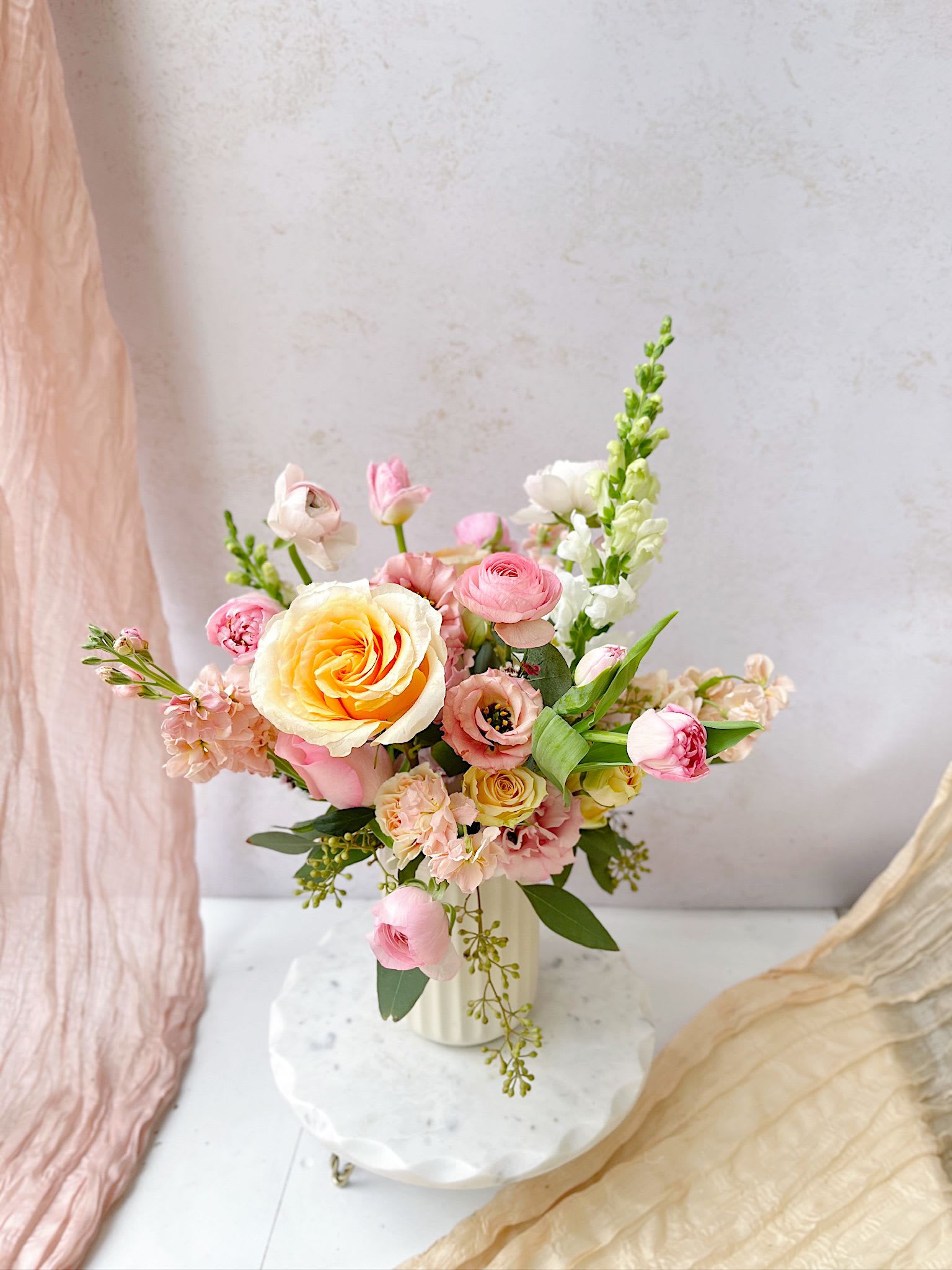 Because of You - A soft and radiant spring vase arrangement featuring roses, ranunculus, tulips, lisianthus, and delicate seasonal blooms in blush, peach, and yellow tones. Designed in a modern, airy style with lush greenery, this Mother’s Day floral arrangement brings warmth, elegance, and a fresh garden feel to any space.  Perfect for gifting, brunch tables, or celebrating loved ones with timeless beauty.